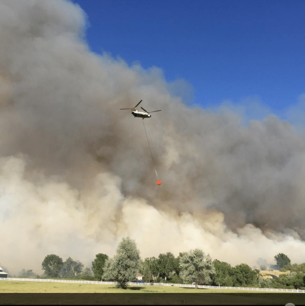 CH-47D Chinook helicopter flying above a wild fire carrying water bucket